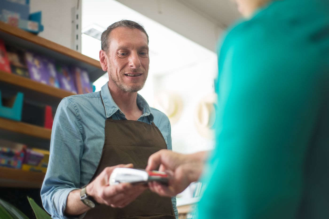 Customer tapping a bank card on a payment terminal at a shop counter